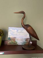 Side view of wood and iron bird sculpture with coastal oil painting behind it