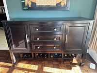 Front view of dark wooden sideboard with two cabinet doors, three central drawers, and wine storage cubbies at the bottom filled with bottles.
