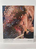 Front cover of the art book showing a large pixelated portrait painting by Chuck Close and an artist painting it.