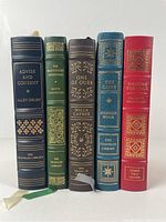 Five leather-bound books standing upright showing spines with titles and decorative gilt work.