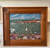 Full front view of the framed waterfront folk painting showing the detailed village, boats, and sky scene with carved heart corners on the wood frame.