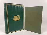 Two vintage travel books side by side: larger green hardcover with gold embossed Egyptian temple design, smaller dark green hardcover with gold lettering on spine, next to a water bottle for scale.