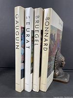 Four art monographs standing upright showing spines, titled Gauguin, Seurat, Bruegel, and Bonnard, all published by Abrams.