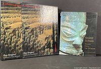 Both books standing upright showing front covers and slipcase of one volume. Terracotta Army and bronze mask images visible.