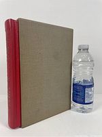 Photo showing book with beige cloth-covered boards and red leather spine next to a water bottle for size comparison.