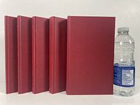 Front view of 5 red hardcover volumes without dust jackets, showing uniform bindings and size next to a water bottle for scale.