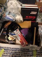 Full view of assorted items including belts, fabrics, nail care tool, jewelry barrettes and McMafia book in box.