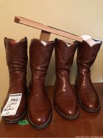 Front view of both pairs of brown Justin leather boots, showing polished leather and clean soles, alongside boot shapers.