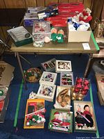 Full table display of assorted Christmas decorations including boxed ornaments, dolls, and light sets