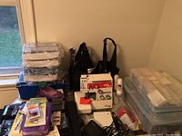 Full view showing sewing machine, large blue and clear plastic storage boxes, and smaller packets of sewing tools, notions, and crafting supplies arranged on a black surface.