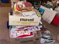 Wide view showing a cardboard box with multiple small craft items including sticker sheets, scissors, and tape placed inside and around it.