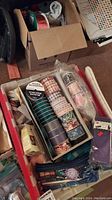 View of boxed assortment of ribbons including floral and striped patterns, stored in a cardboard box and plastic container