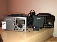 Two audio receivers side by side on a surface with power adapters and cords behind them