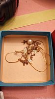 Blue box containing tangled gold chains and a pearl earring