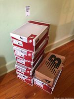 Stack of six New Balance shoeboxes in various sizes and styles shown. Boxes are placed in a column on the floor.