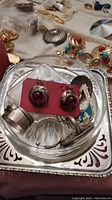 Photo of sterling silver earrings on red holder, ring and small silver container displayed on clear glass dish.