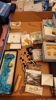 Overview of assorted jewelry in cardboard box with small boxes and packages