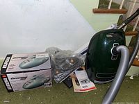 View of Eureka Copperhead Plus box and green Miele Complete C3 canister vacuum with attached hose, tool bag and manuals