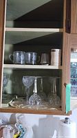 Cabinet shelf showing two glass mugs and four upside-down crystal wine glasses.