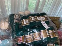 Multiple skeins of dark green Bernat yarn, packaged in plastic bags.