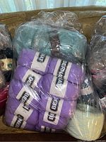 Bag of purple Bernat yarn skeins wrapped in plastic, with visible Bernat labels.