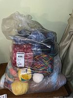 Large clear plastic bag filled with assorted yarn and thread including fuzzy cones, variegated balls, and small skeins