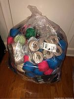 Plastic bag full of yarn skeins and cones showing bright colors like blue, red, green, and neutral colors, sealed with a sticker.