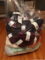 Large clear plastic bag filled with multiple skeins of Patons Canadiana yarn in several colors including maroon, black, cream, orange, and light blue.