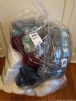 Clear plastic bag containing multiple skeins of yarn in various colors including white, gray, dark blue, and burgundy, some labeled Patons.