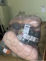Large clear bag containing multiple skeins of yarn in pale pink and black-white colors on a couch.