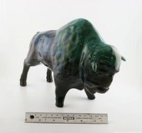 Front angled view of ceramic buffalo with ruler for scale showing glossy glaze with blue-green-black coloration and iridescence.
