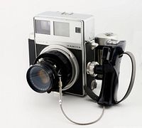 Camera body with lens mounted and pistol grip attached, front three-quarter view