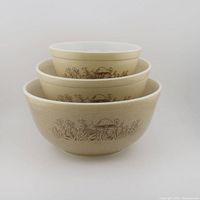 Three nested Pyrex mixing bowls showing the Forest Fancies mushroom pattern on a speckled brown background.