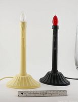 Two vintage plastic bulb candles, one white with clear bulb, one black with red bulb, with a ruler for size reference.