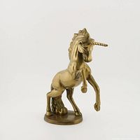 Front angle view of the solid brass unicorn figurine showing the unicorn rearing with detailed mane and tail, mounted on a brass base with screws visible.