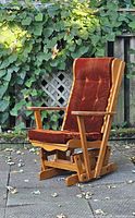 Side view of vintage solid maple rocking chair with orange tufted cushions set outdoors showing wood grain and rocking base