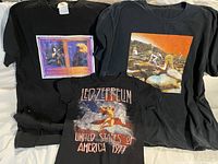 Three black Led Zeppelin T-shirts laid out on a surface, showing front prints with album and tour designs.