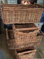 Side view of stacked four rectangular wicker baskets with wooden handles showing woven texture and handle details.