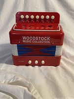 Front view showing red body and Woodstock Music Collection branding with white buttons and blue bellows.