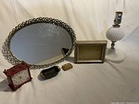 Full view of all four items together: brass filigree oval tray, Jerger red clock, brass ashtray, and hobnail lamp base