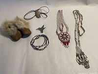 Full lot overview showing all items on white background including moccasins, beaded necklaces, bracelets, bird pin, and cord.