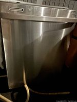 Front view of the stainless steel Kenmore dishwasher showing exterior condition and attached hose.