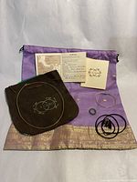 Photo of all jewelry items laid out on purple decorative fabric including metal wire necklace, bracelet, small ring, black cords, brown velvet pouch with LaCano logo, and two certificates.