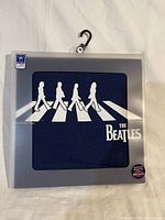 Navy blue Beatles T-shirt folded in packaging with white silhouette of band crossing Abbey Road and The Beatles logo