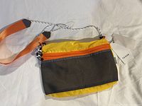 Front view of Taikan crossbody bag showing yellow fabric, black mesh front pocket, and orange zipper with adjustable strap extending.