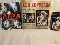 Three Led Zeppelin items, a large coffee table book, another book, and a magazine arranged on a surface.