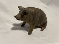 Front left angled view of cast iron sitting piggy bank showing texture, wear, and patina.