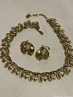 Full view of the Trifari gold tone necklace and matching earrings set laid flat showing pearls and rhinestones