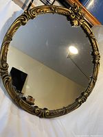 Round mirror with ornate gold wood frame, showing full mirror surface and frame.