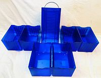 Photo of six blue plastic CD storage compartments arranged on a white surface showing front and side structure with a handle on the tall central piece